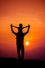 Fototapeta premium silhouette of a family with a boy riding his father's neck happily against the sunset sky