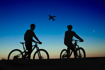 Obraz na płótnie Canvas Two cyclists on the background of night sky and moon, watching the plane