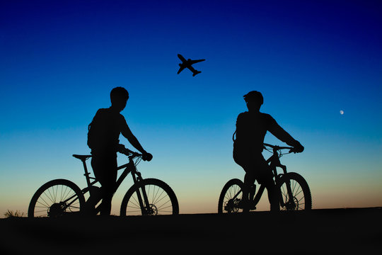Two cyclists on the background of night sky and moon, watching the plane