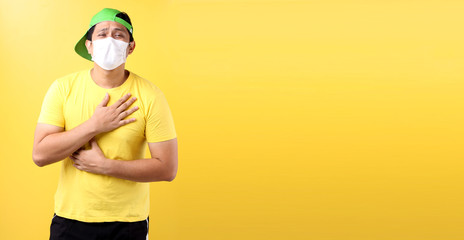 Asian man feel pain on lung and wear protective mask pollution or transmissible infectious diseas and coronavirus or covid-19, healthcare and illness concept.on yellow background in studio for ads.