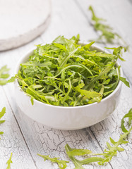 Fresh green arugula leaves on white bowl, rucola rocket salad on wooden rustic background with place for text. Selective focus,  healthy food, diet. Nutrition concept