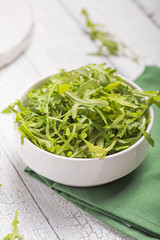 Fresh green arugula leaves on white bowl, rucola rocket salad on wooden rustic background with place for text. Selective focus,  healthy food, diet. Nutrition concept