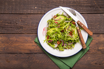 Fresh green arugula leaves on white bowl, rucola rocket salad with apple, radish, pecan nuts, onion on wooden rustic background with place for text. Top view,  healthy food, diet. Nutrition concept