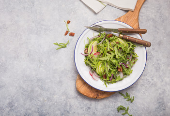 Fresh green arugula leaves on white bowl, rucola rocket salad with apple, radish, pecan nuts, onion on wooden rustic background with place for text. Top view,  healthy food, diet. Nutrition concept
