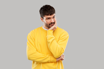 people concept - sad young man in yellow sweatshirt thinking over grey background