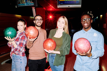 Successful intercultural bowling players with balls standing in front of camera
