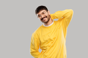 people concept - smiling young man in glasses and yellow sweatshirt over grey background
