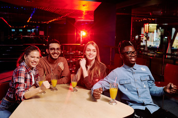 Four young happy intercultural bowling fans having drinks and looking at players