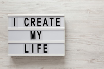 'I create my life' words on a lightbox on a white wooden background, top view. Overhead, from above, flat lay. Copy space.
