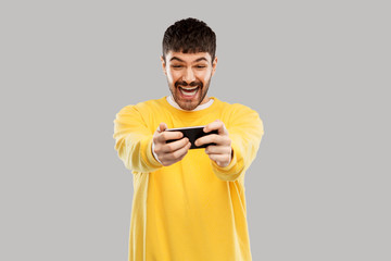 technology, communication and people concept - happy laughing young man playing game on smartphone over grey background