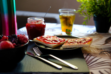 Sweet breakfast with freshly made jam on toast and a very hot tea or honey camomile served by a girl. She also spreads the jam