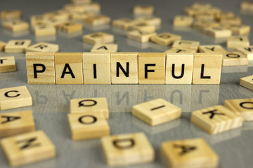 word painful is made of square wooden letters on a gray background