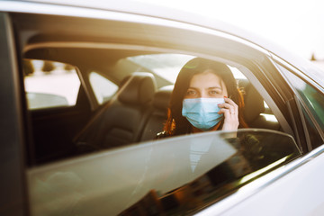 Girl in protective sterile medical mask on her face is  talking on his phone in taxi. The concept of preventing the spread of the epidemic and treating coronavirus, pandemic in quarantine city.