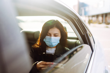 Girl in protective sterile medical mask on her face is  talking on his phone in taxi. The concept...