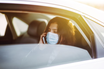 Girl in protective sterile medical mask on her face is  talking on his phone in taxi. The concept of preventing the spread of the epidemic and treating coronavirus, pandemic in quarantine city.