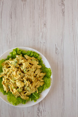 Homemade Coronation Chicken Salad on a white plate on a white wooden table, top view. Flat lay, from above, overhead.