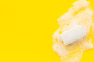 Soap bar with foam on yellow background top-down copy space
