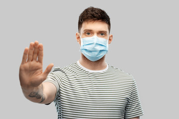 health protection, safety and pandemic concept - young man in protective medical mask making stop gesture over grey background