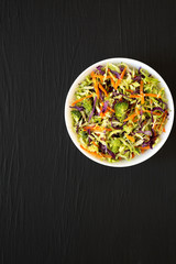 Homemade Raw Shredded Broccoli Slaw in a white bowl on a black background, top view. Copy space.