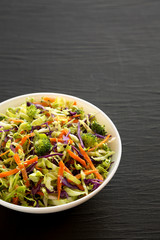 Homemade Raw Shredded Broccoli Slaw in a white bowl on a black surface, low angle view. Copy space.