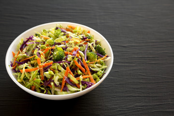 Homemade Raw Shredded Broccoli Slaw in a white bowl on a black surface, side view. Copy space.