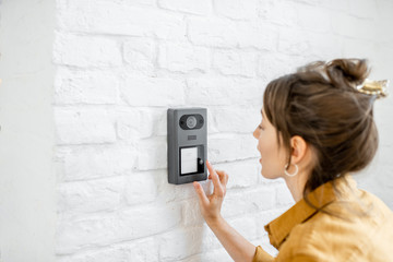Woman rings the house intercom with a camera installed on the white brick wall