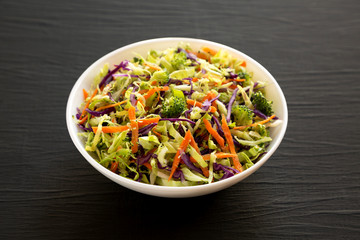 Homemade Raw Shredded Broccoli Slaw in a white bowl on a black background, side view. Close-up.