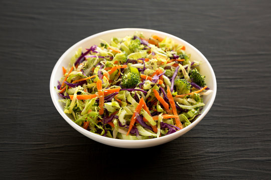 Homemade Raw Shredded Broccoli Slaw In A White Bowl On A Black Background, Side View. Close-up.