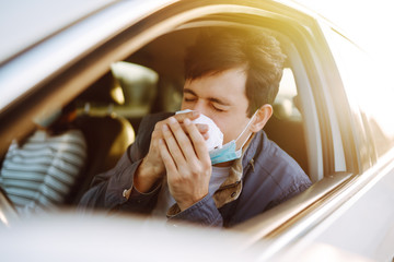 Young man coughing and sneezing into a handkerchief while driving a car. The concept of preventing...