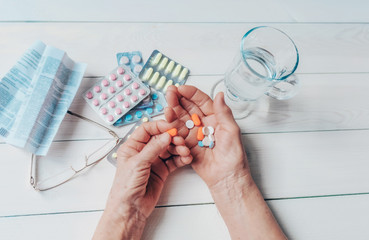 Senior hands with pills and drugs on table, glass of water. Wrinkled hands of old woman holding...