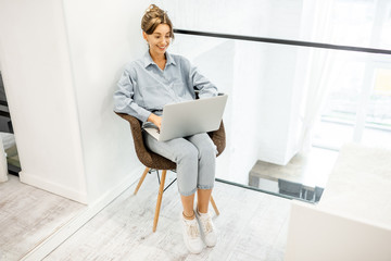 Young woman working on laptop while sitting on the comfortable chair at home. Work online from home at cozy atmosphere concept