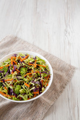 Homemade Raw Shredded Broccoli Slaw in a white bowl on cloth, low angle view. Copy space.