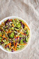 Homemade Raw Shredded Broccoli Slaw in a white bowl on cloth, top view. Overhead, from above, flat lay. Space for text.