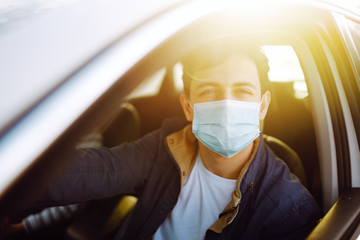 Young man in protective sterile medical mask driving car. The concept of preventing the spread of...