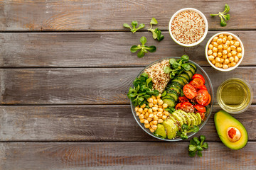 Veggie bowl. Vegetable salad with quinoa, avocado, tomato, spinach and chickpeas - on wooden table. Top view copy space