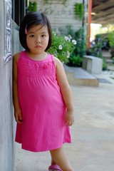 A cute little Asian girl sulking, feeling unhappy, leaning against a wall, frowning. Making funny faces.