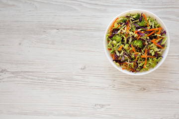 Homemade Raw Shredded Broccoli Slaw in a white bowl on a white wooden surface, top view. Overhead, from above, flat lay. Copy space.
