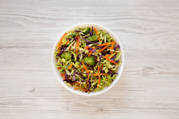 Homemade Raw Shredded Broccoli Slaw in a white bowl on a white wooden background, top view. Overhead, from above, flat lay.