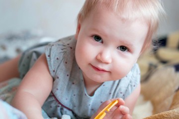 Fototapeta premium Little cute girl of Caucasian appearance. Cute baby with a blond moor. She is dressed in a gray dress. In a home atmosphere. Home clothes. Child 1 year. Cheerful girl playing.