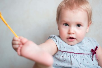 Little cute girl of Caucasian appearance. Cute baby with a blond moor. She is dressed in a gray dress. In a home atmosphere. Home clothes. Child 1 year. Cheerful girl playing.