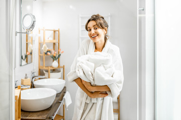 Young woman in bathrobe doing some housework, standing with towels in the bathroom