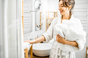 Young woman in bathrobe doing some housework, standing with towels in the bathroom