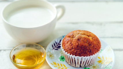 Close up banana cake on white plate with honey and cup of milk on wooden table.