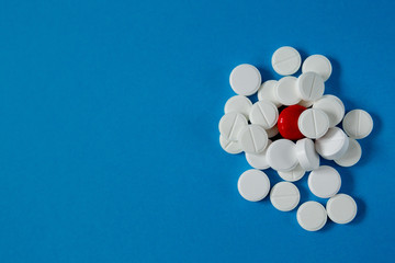 heap of white pills and one red, on a blue background