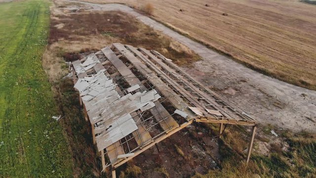 Aerial: flying around an abandoned farm with a partially destroyed roof. Ruins of an old industrial building for farm animals in the evening. Prerequisites for designing a crisis