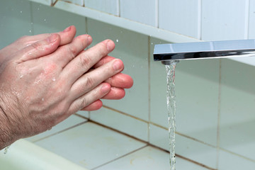 a man washes his hands with soap and water under the tap in a bathroom