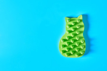Green rubber brush for caring for animal on blue background. Concept of grooming for pet fur