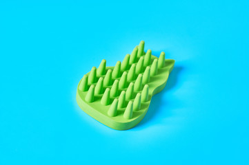 Green rubber brush for caring for animal on blue background. Concept of grooming for pet fur