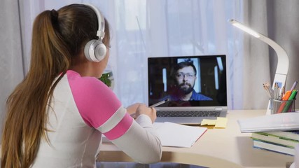 Girl with headphones learning online on computer, communicate with teacher, writing, distance education due quarantine time