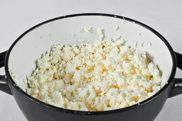 White cottage cheese in a black bowl. lots of cheese on a white background.